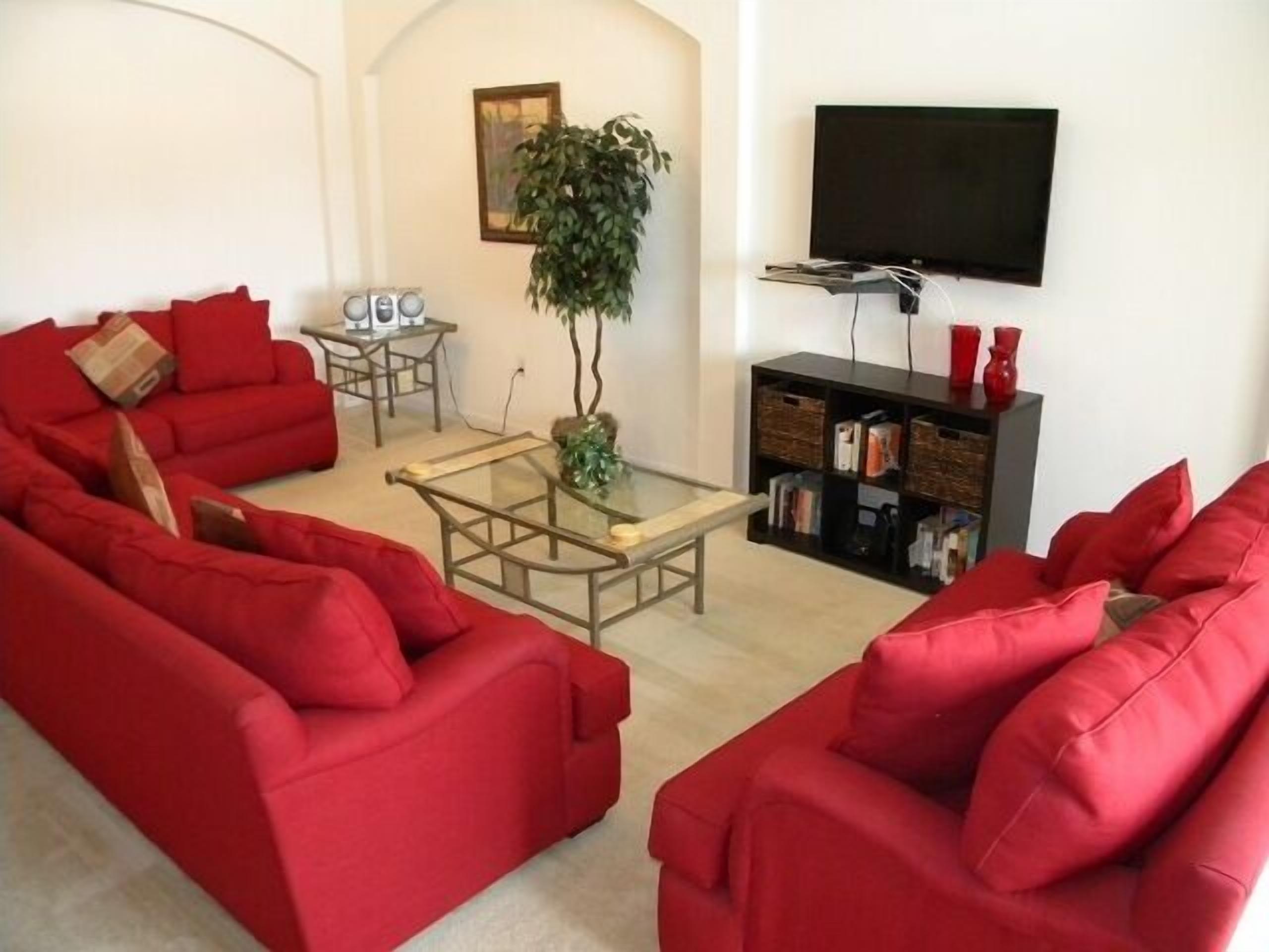 A living room with red sofas, a glass coffee table, a bookshelf, a TV, and a plant.