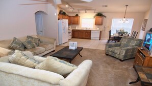 A living room with a sofa, armchair, and coffee table. There is a kitchen in the background with wooden cabinets and a refrigerator. - Bjw538 - Sandy Ridge - 4 Bed 3 Baths Villa (Davenport)