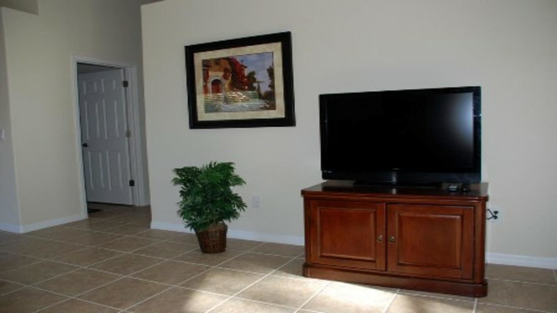 A living room with a flat-screen TV on a wooden cabinet, a framed picture on the wall, and a potted plant.