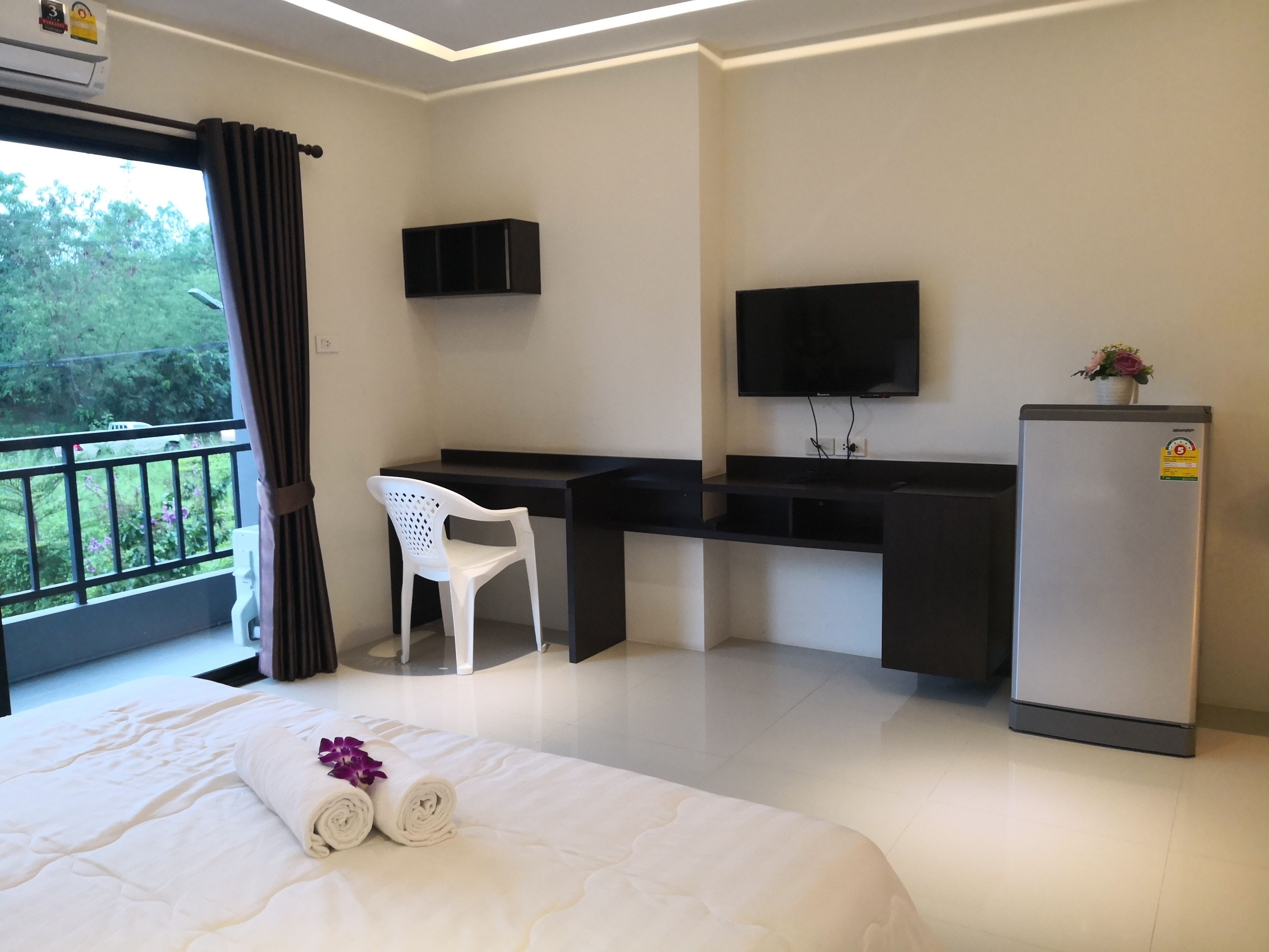 A hotel room with a bed, a desk, a chair, a TV, and a refrigerator.