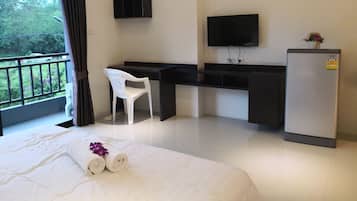 A hotel room with a bed, a desk, a chair, a TV, and a refrigerator.