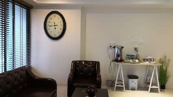 A living room with a brown leather sofa, a coffee table with a vase, a clock on the wall, and a small table with a kettle and other items.