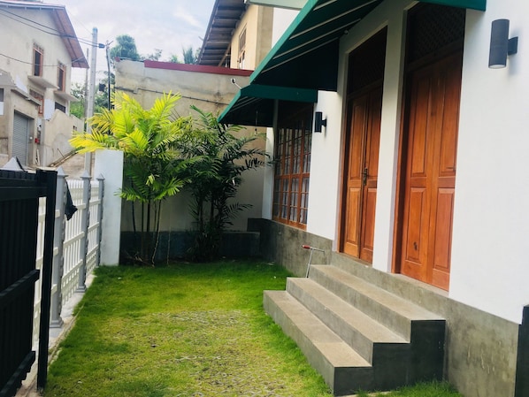 A residential area with a white house, a wooden door, and a small garden with steps leading to the entrance.