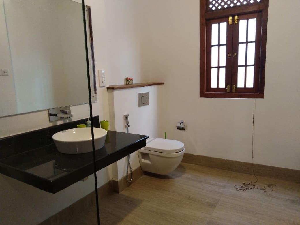 Un baño con encimera negra, lavamanos blanco, inodoro blanco y ventana con marco de madera.