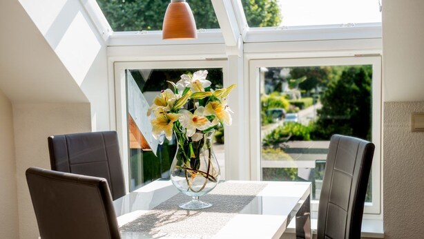 A dining area with a table and chairs, a vase of flowers, and a view through large windows. - Boutique Lodgings Horster (Bensheim)