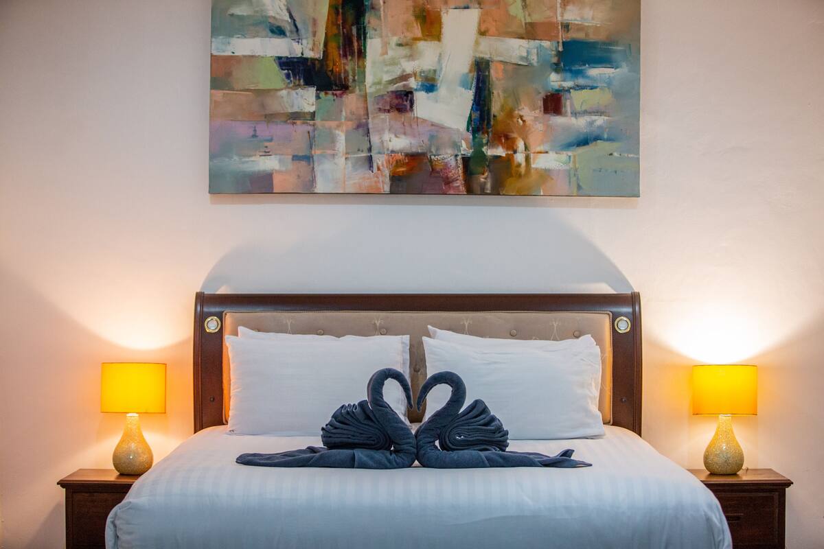 A hotel room with a bed, two bedside lamps, and a painting on the wall.