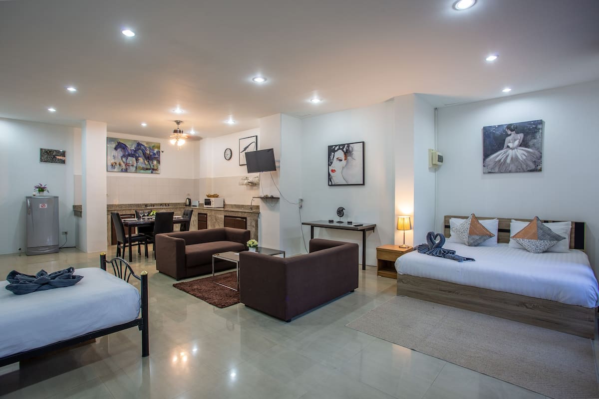 A modern hotel room with a bed, a sofa, a dining area, and a TV.