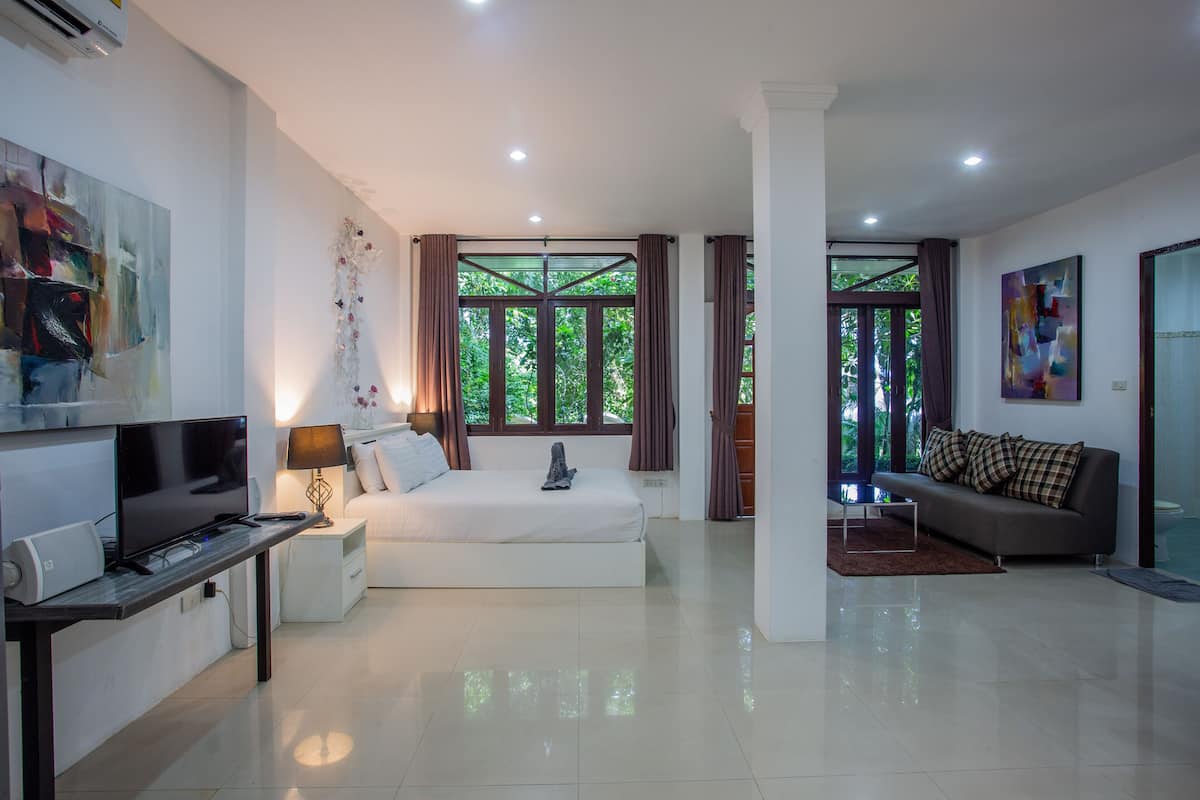 A modern hotel room with a large bed, a sofa, a TV, and artwork on the walls.