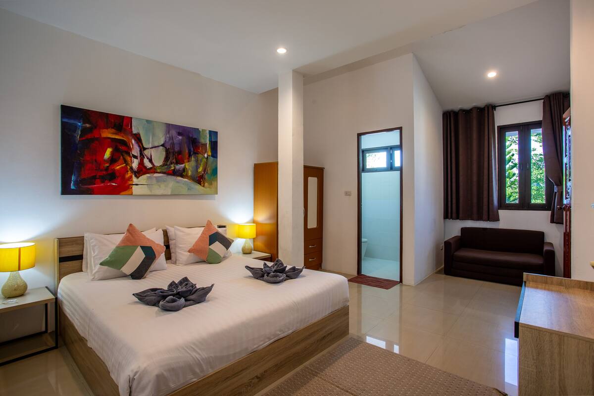 A modern hotel room with a large bed, a painting on the wall, a sofa, and a view of the outdoors.