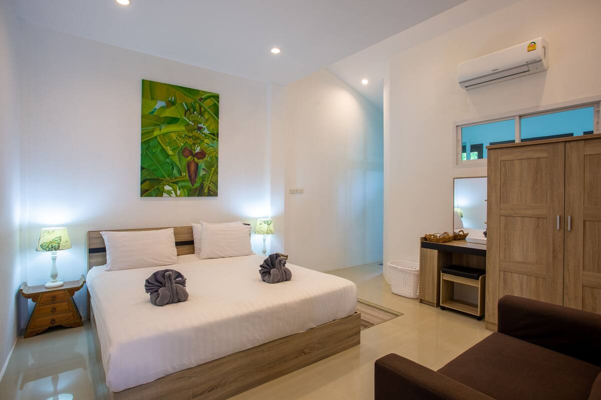 A modern hotel room with a large bed, a desk, and an air conditioning unit.