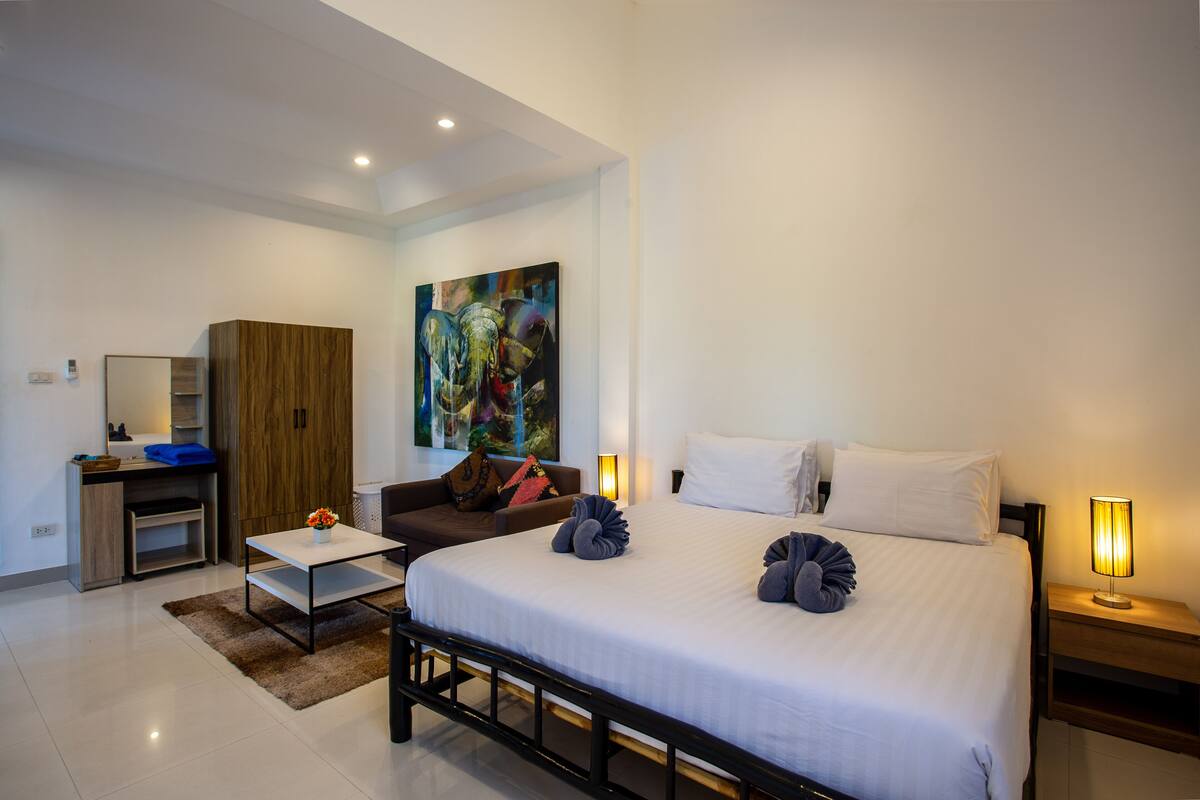 A modern hotel room with a large bed, a desk with a chair, a wardrobe, and a painting on the wall.
