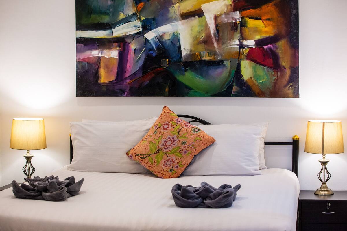 A neatly made bed with two pillows, a floral-patterned pillow, and two bedside lamps.