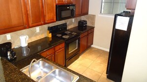 Una cocina con armarios de madera, un microondas negro, una estufa y un refrigerador.