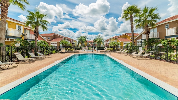 A rectangular swimming pool with clear blue water, surrounded by lounge chairs and palm trees, with buildings in the background. - Aco66067 - Lake Berkley - 4 Bed 2 Baths Villa (Kissimmee)