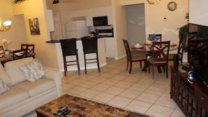 A living room with a sofa, coffee table, and TV stand. There is a kitchen in the background with a microwave and cabinets. - Aco66067 - Lake Berkley - 4 Bed 2 Baths Villa (Kissimmee)