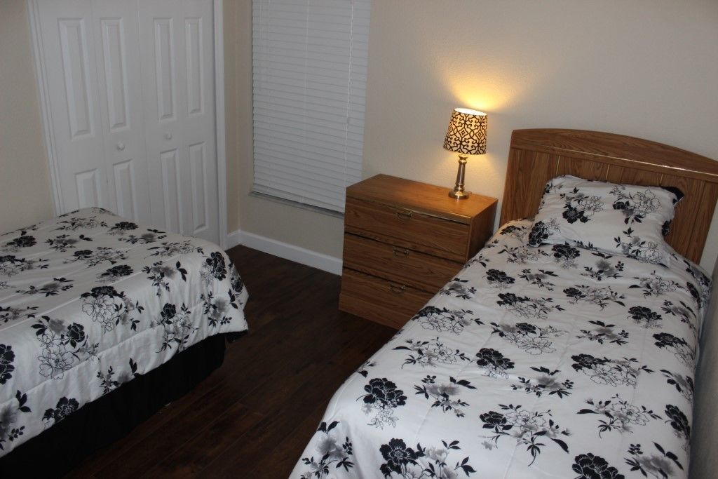 A bedroom with two single beds, a nightstand with a lamp, and a white door.