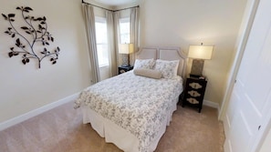 A bedroom with a bed, two bedside tables, a wall-mounted decorative piece, and a window with curtains. - Aco231262 - The Encore Club Resort - 6 Bed 5.5 Baths Villa (Kissimmee)