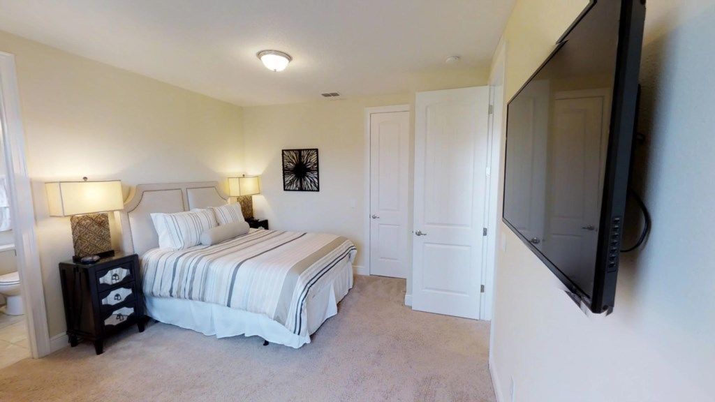 Une chambre à coucher avec un lit, des tables de chevet, un téléviseur et une porte.