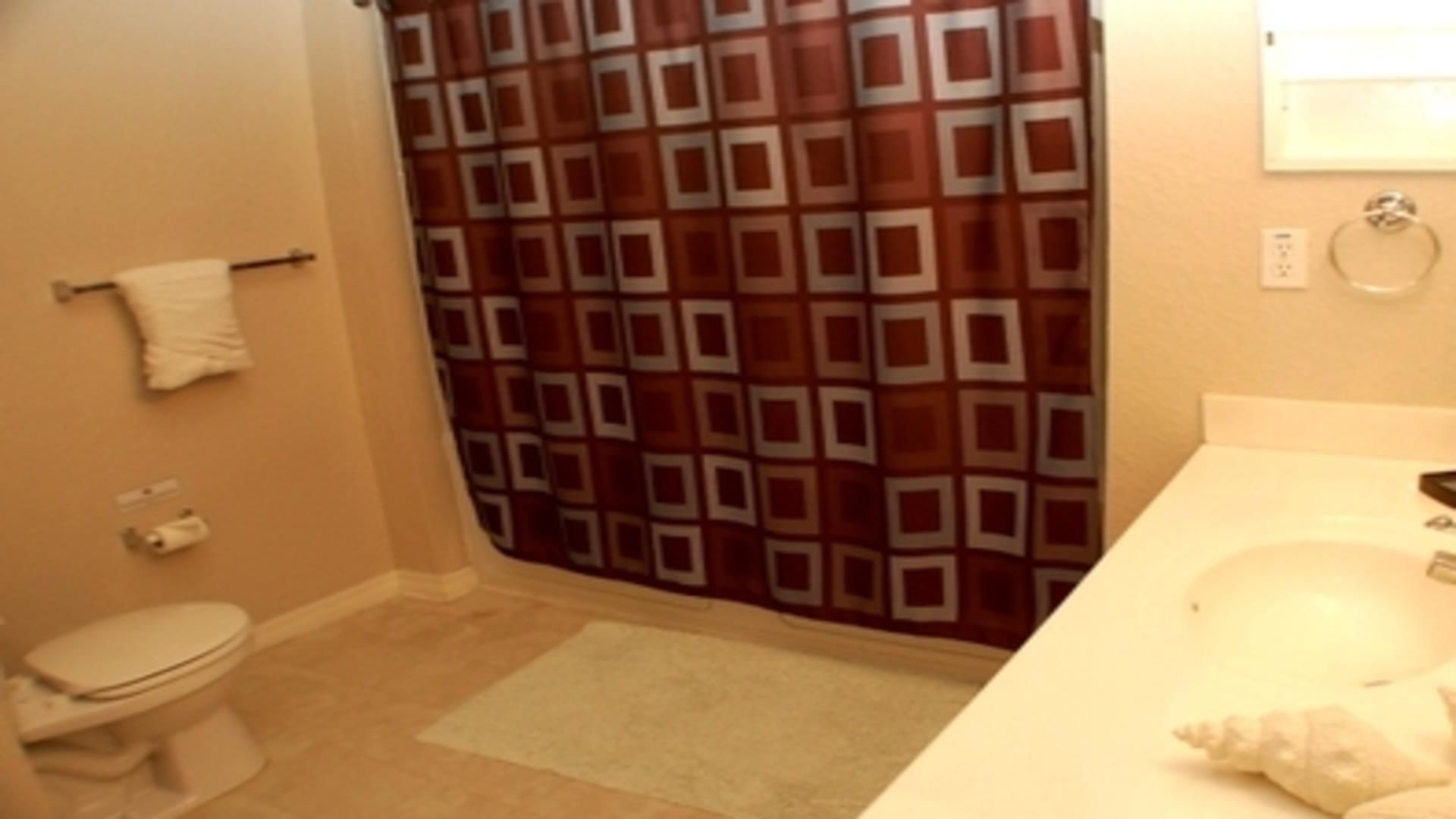 A bathroom with a patterned shower curtain, a toilet, a sink, and a towel rack.