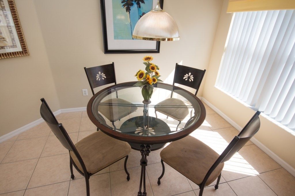 A dining area with a glass table surrounded by four chairs, a vase with sunflowers, and a pendant light.