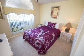 Une chambre à coucher avec un lit, une table de chevet, une lampe et une fenêtre avec des stores.