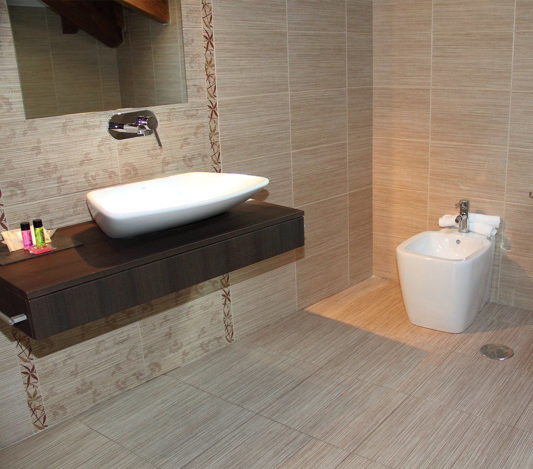 A modern bathroom with a large mirror, a white vessel sink, and a bidet.