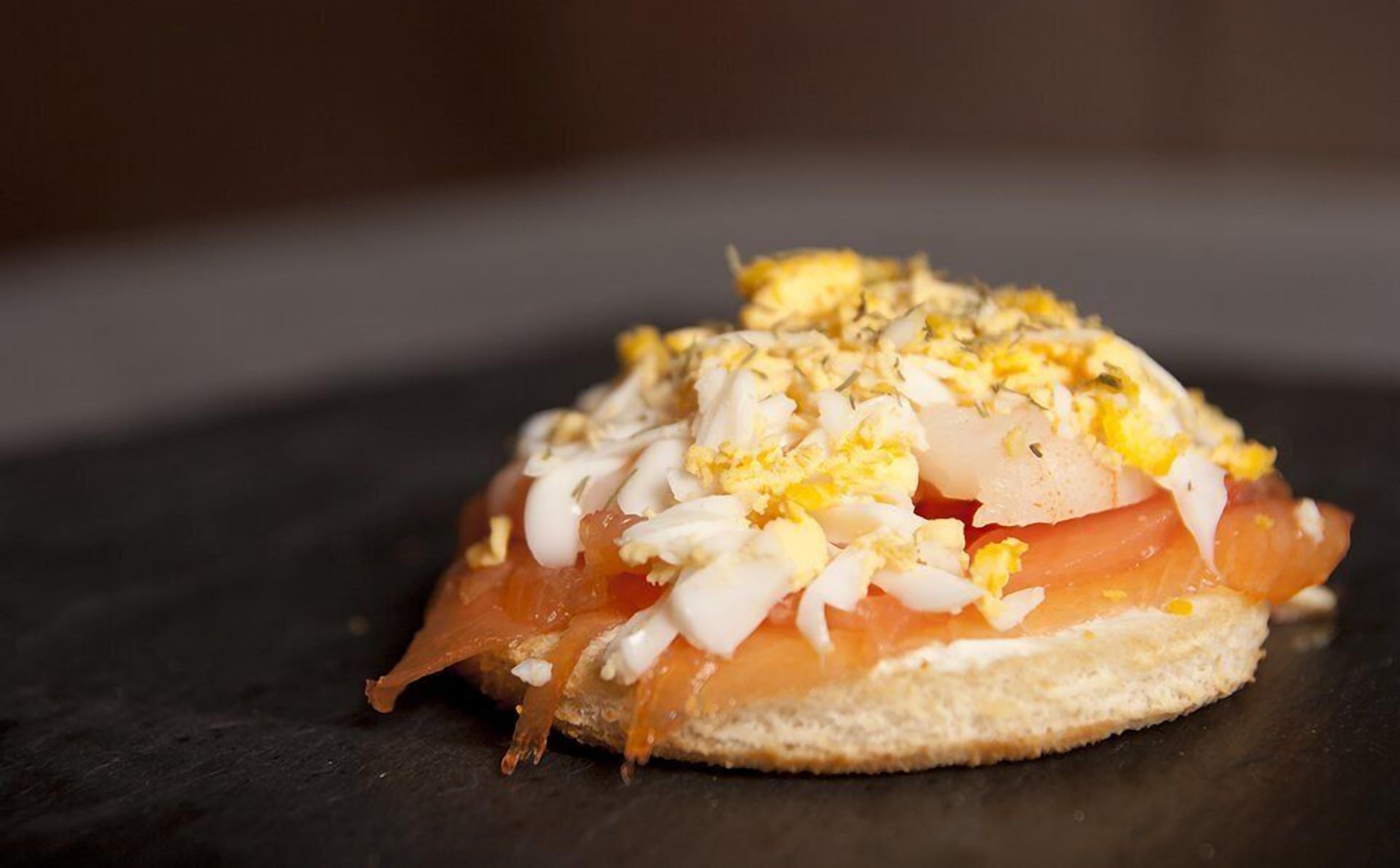 Een sandwich met zalm, eieren en uien op een sneetje brood.