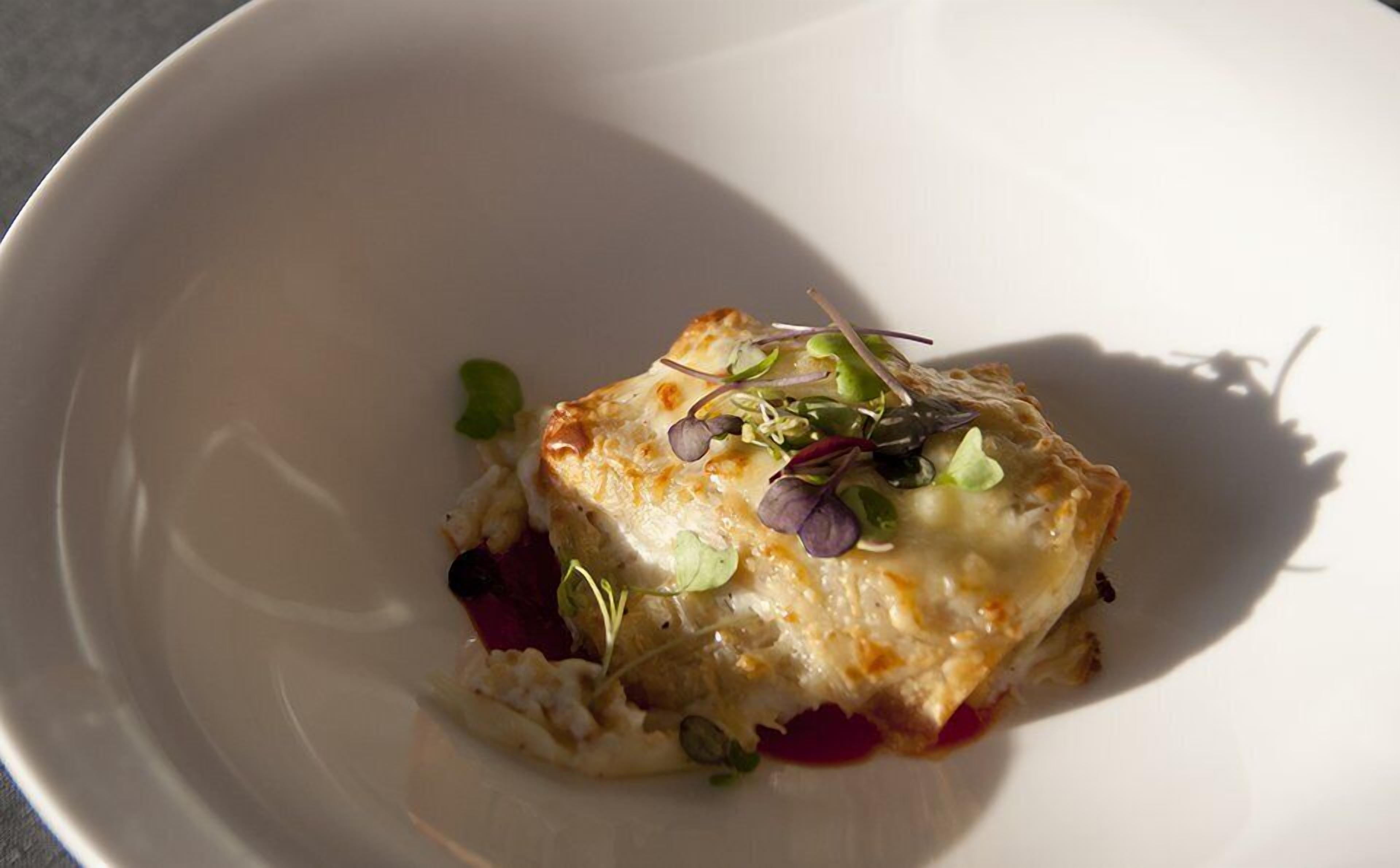 Un plato con costra dorada, cubierto de vegetales y salsa roja.