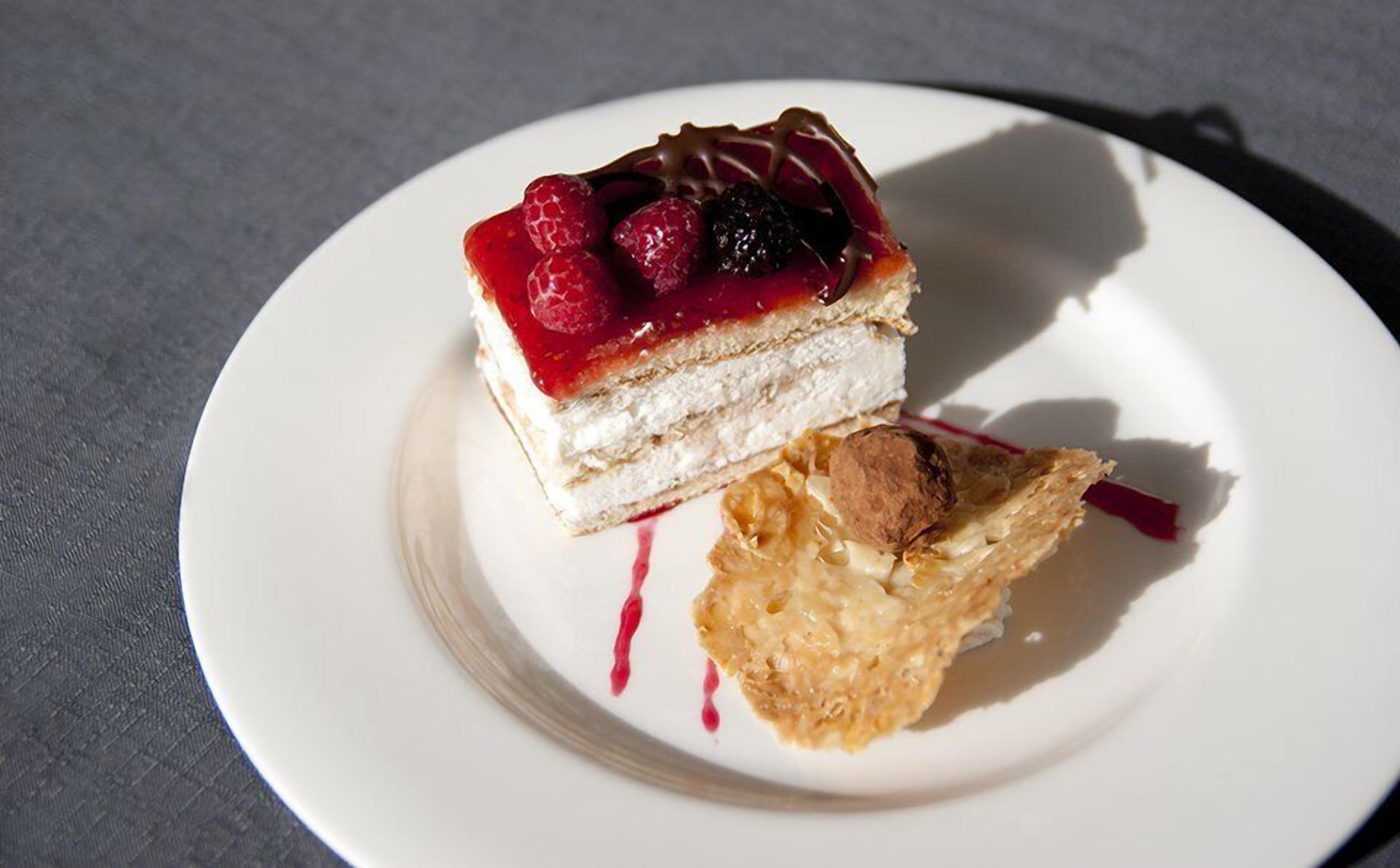Un postre sobre un plato blanco, con cobertura de frutos rojos y una porción de pastel.