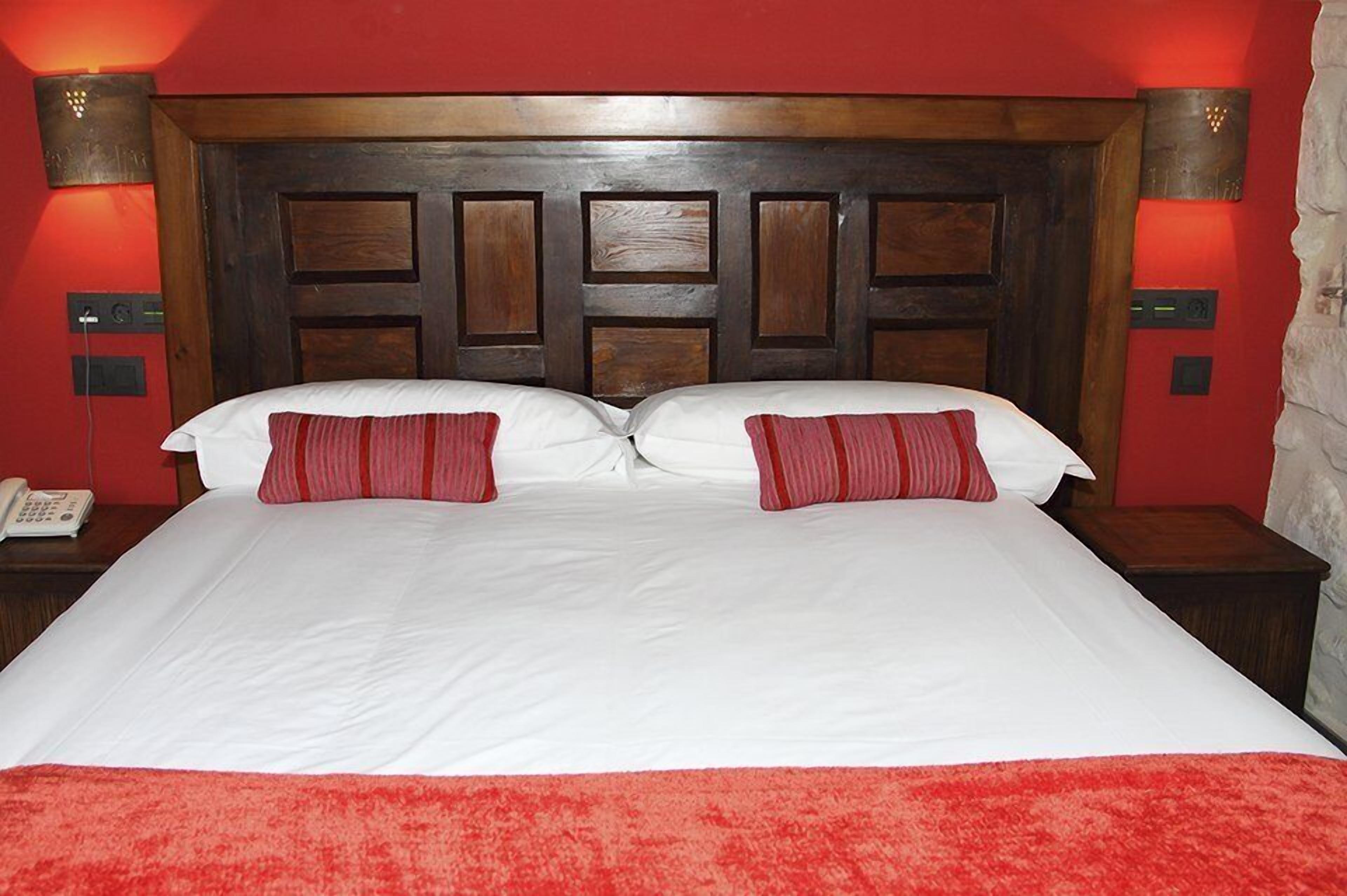 A double bed with a wooden headboard, two red pillows, and a red carpet.