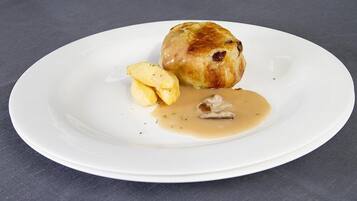 A white plate with a baked item, possibly a meatball, accompanied by a small portion of mashed potatoes and gravy.
