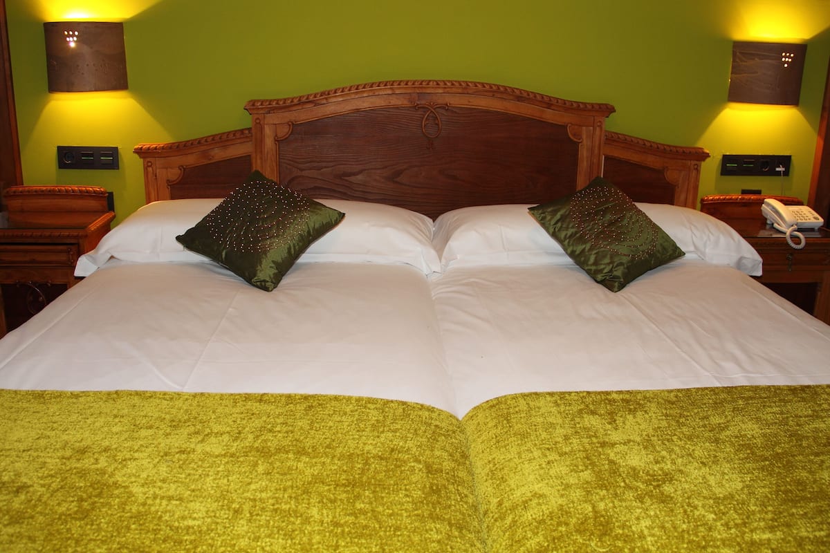A double bed with two pillows, a wooden headboard, and a green bedspread.