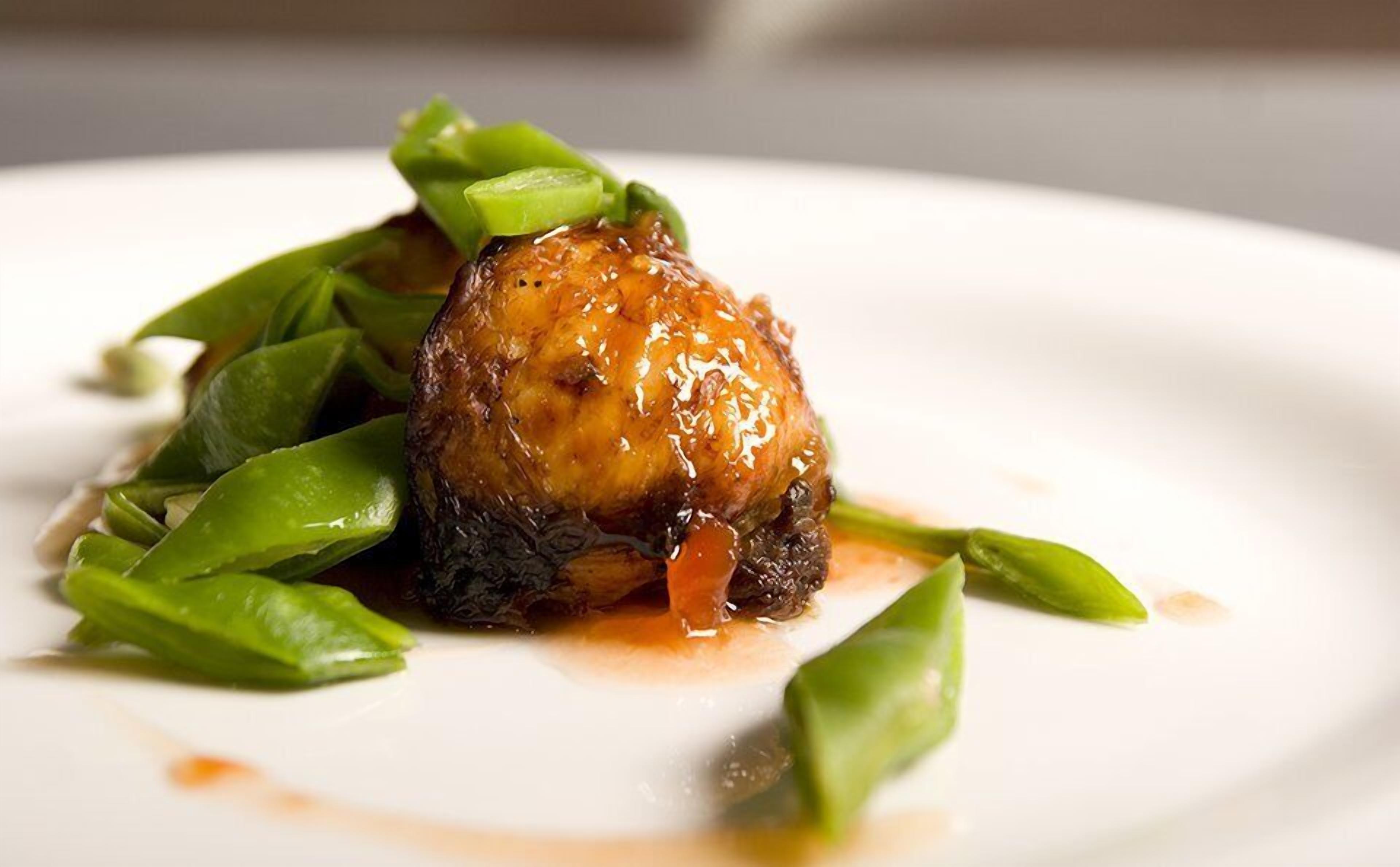 Un plato con un guiso de carne brillante y verduras verdes.