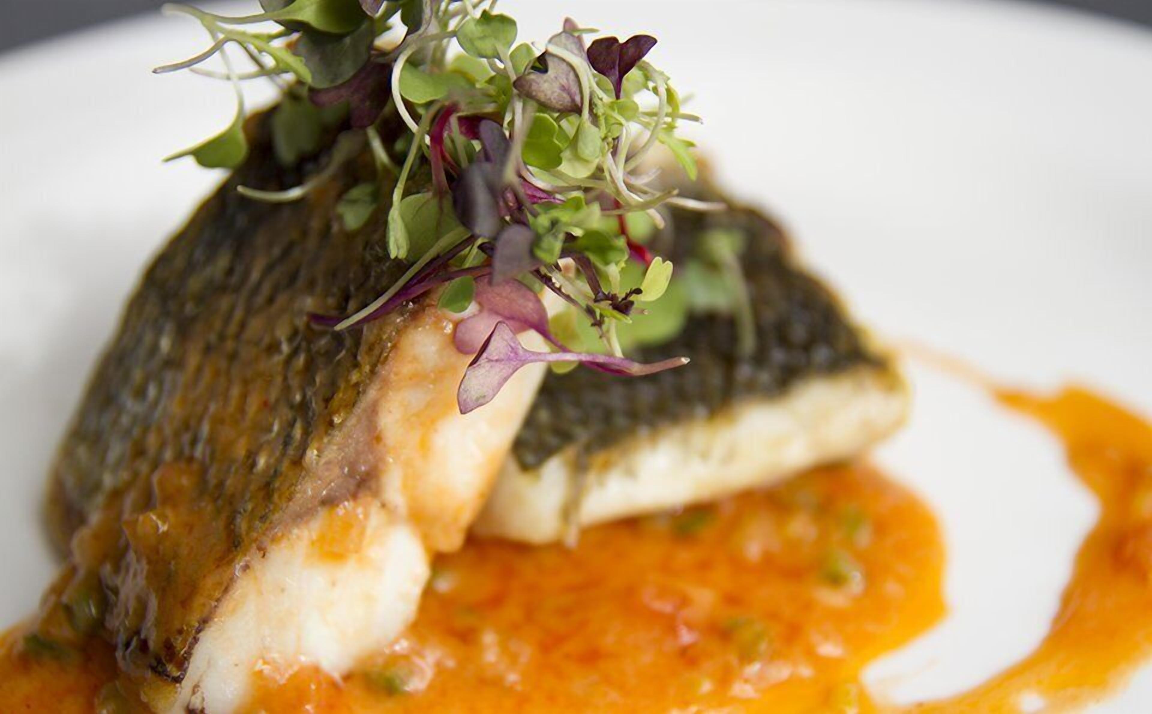A fish dish with a sauce and greens on a plate.