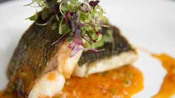 A fish dish with a sauce and greens on a plate.