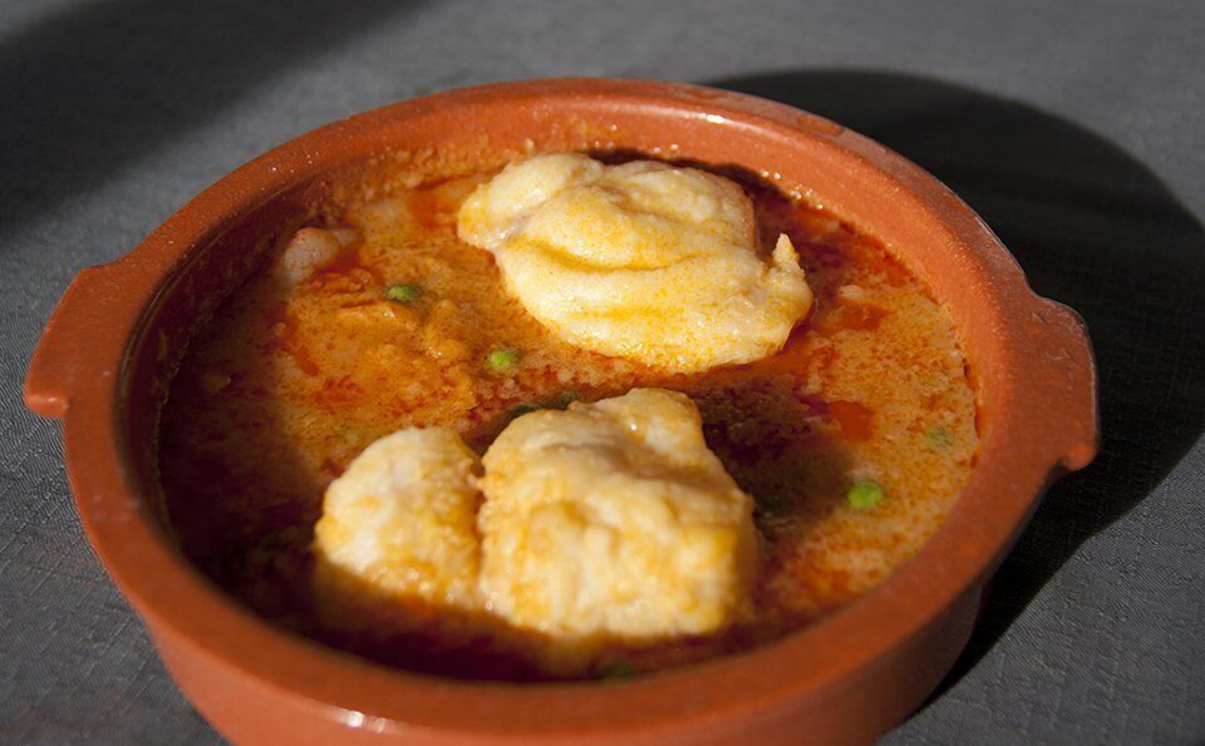 Una olla de barro con dos porciones de comida, posiblemente un estofado o curry, con hierbas verdes visibles.