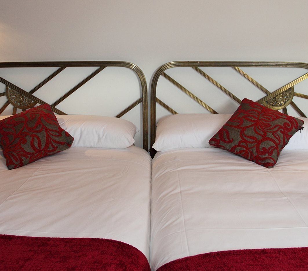 Un lit double avec une tête de lit en métal, deux oreillers à motifs rouges et gris, et un plaid rouge.