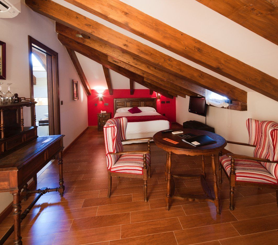 Un dormitorio acogedor en el ático, con techo de madera, una cama, un televisor y sillas a rayas.