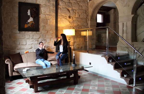 Una habitación de paredes de piedra con una mesa de vidrio, un sofá y una escalera.
