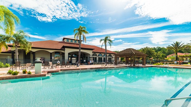 A swimming pool with lounge chairs and palm trees, surrounded by a building with a red-tiled roof. - Aco63671 - Bella Vida Resort - 6 Bed 5.5 Baths Villa (Kissimmee)