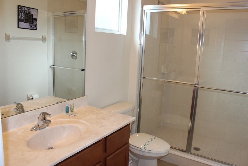 A bathroom with a sink, mirror, toilet, and a glass-enclosed shower area.