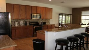 A kitchen with wooden cabinets, a granite countertop, a stainless steel microwave, and a large island with bar stools. - Aco63671 - Bella Vida Resort - 6 Bed 5.5 Baths Villa (Kissimmee)
