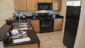 A kitchen with wooden cabinets, a black microwave, a stove, a sink, and a refrigerator. - Ip62813 - Encantada Resort - 2 Bed 2.5 Baths Townhome (Kissimmee)