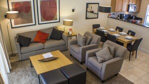 A modern living room with a sofa, two armchairs, a coffee table, and a dining area with a table set for four. - Ip62813 - Encantada Resort - 2 Bed 2.5 Baths Townhome (Kissimmee)