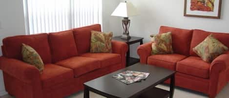 A living room with two red sofas, a dark coffee table, a lamp, and a painting on the wall.
