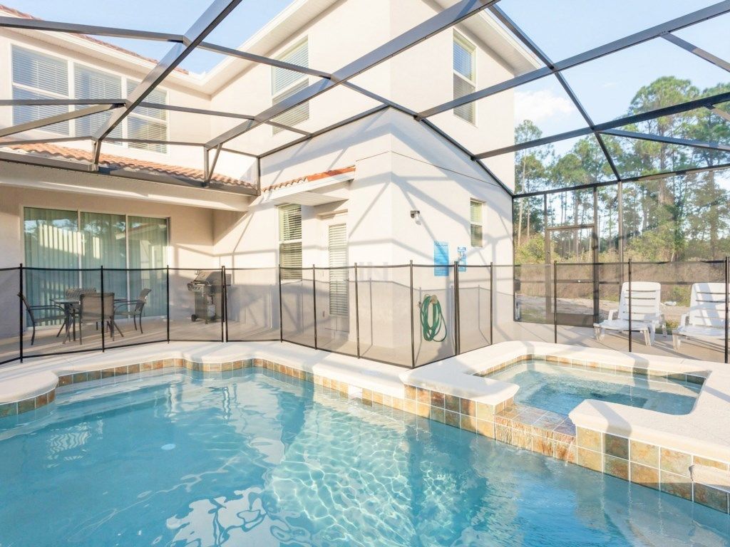 An indoor swimming pool with a glass enclosure, surrounded by a patio area with chairs and a table.