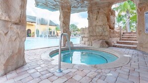 A pool area with a hot tub, surrounded by stone walls and a waterfall feature.
