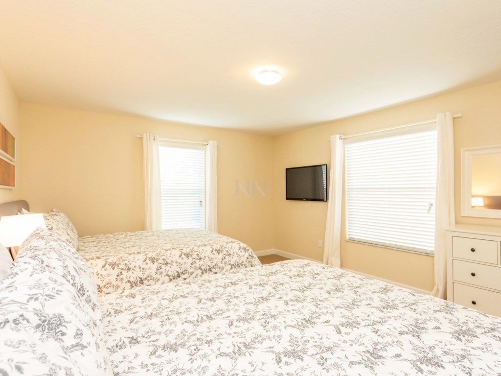 A bedroom with two beds, a TV mounted on the wall, and a dresser with drawers.