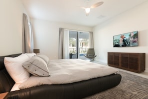 Een moderne slaapkamer met een groot bed, een plafondventilator, een televisie en uitzicht op het balkon.