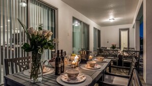 Ein Essbereich mit einem langen Tisch, gedeckt für eine Mahlzeit, mit Blumenstrauß, Kerzen und Weinflaschen.